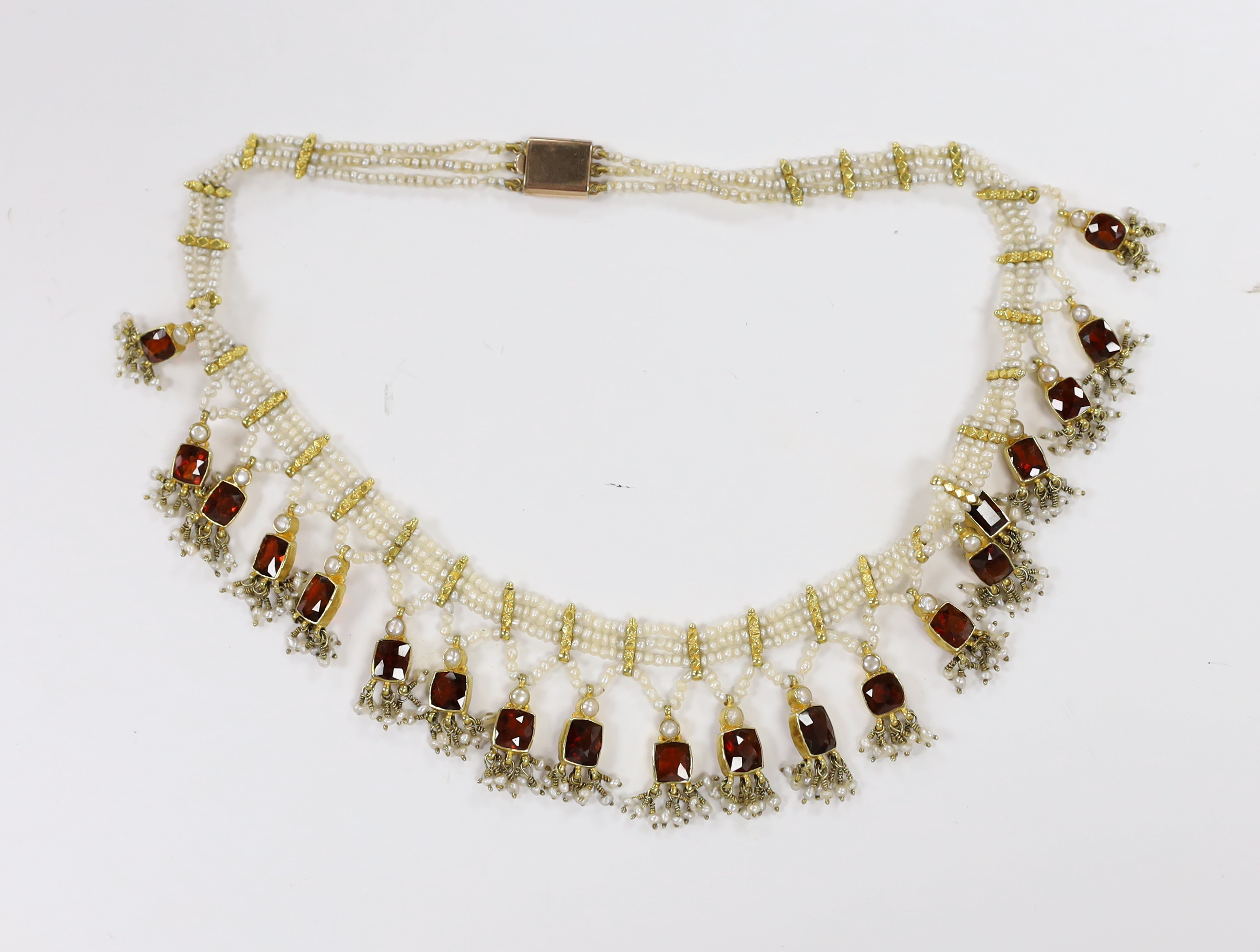 An Indian yellow metal mounted triple strand seed pearl and graduated twenty stone garnet set drop fringe necklace, 40cm.